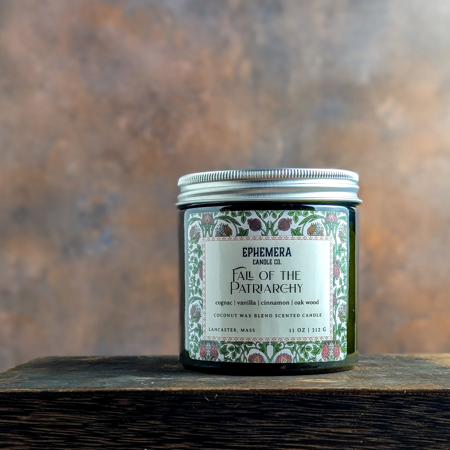 Fall of the Patriarchy candle on a wooden shelf. Cognac, vanilla, cinnamon and oak wood.