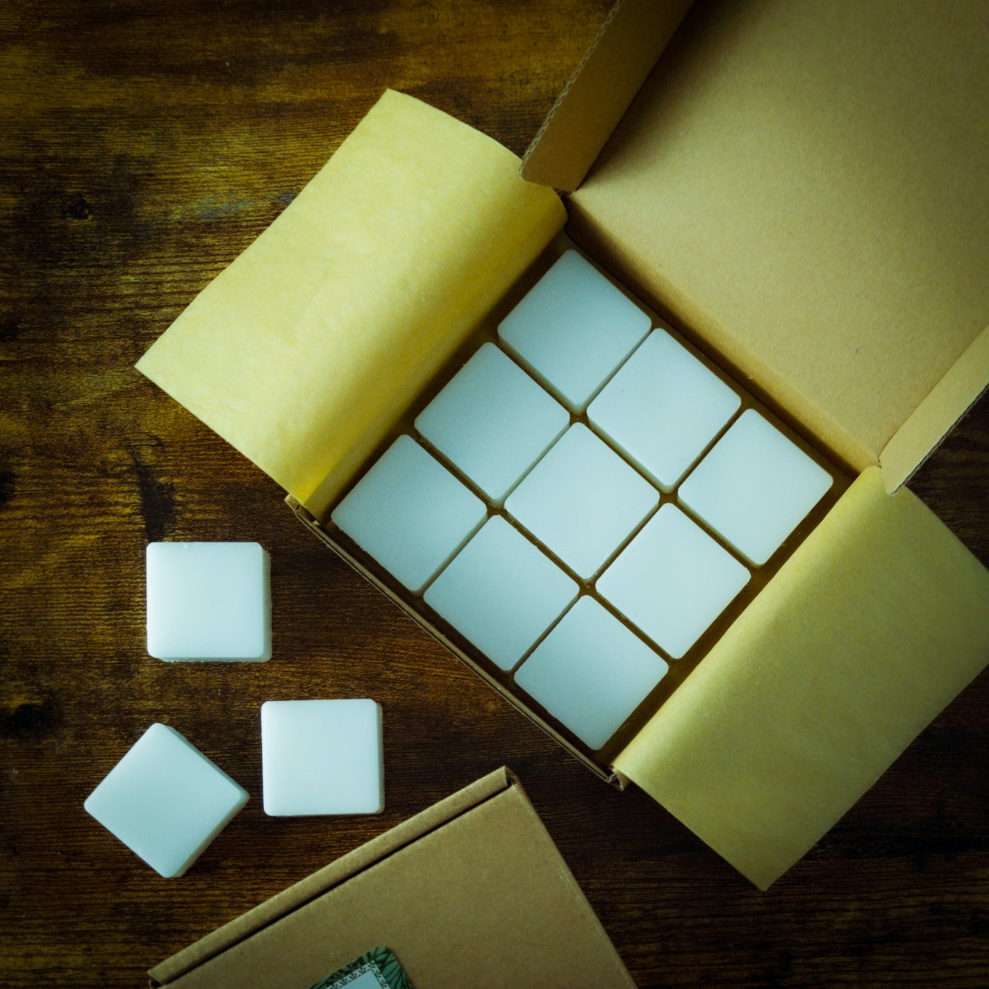 9 wax melt cubes arranged in a box on a table. Three wax melt cubes are scattered on the table near the box.