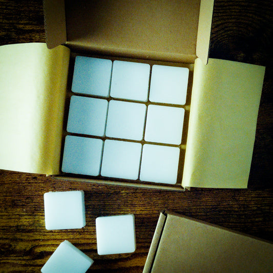 9 square wax melt cubes arranged in a box 3 by 3. Three individual melts are on the table next to the box.