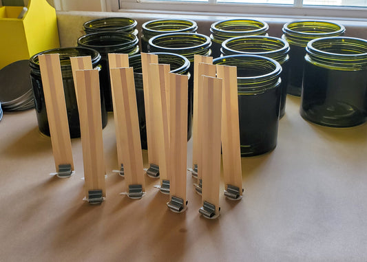 Collection of wooden wicks and green glass candle jars preparing to pour candles.