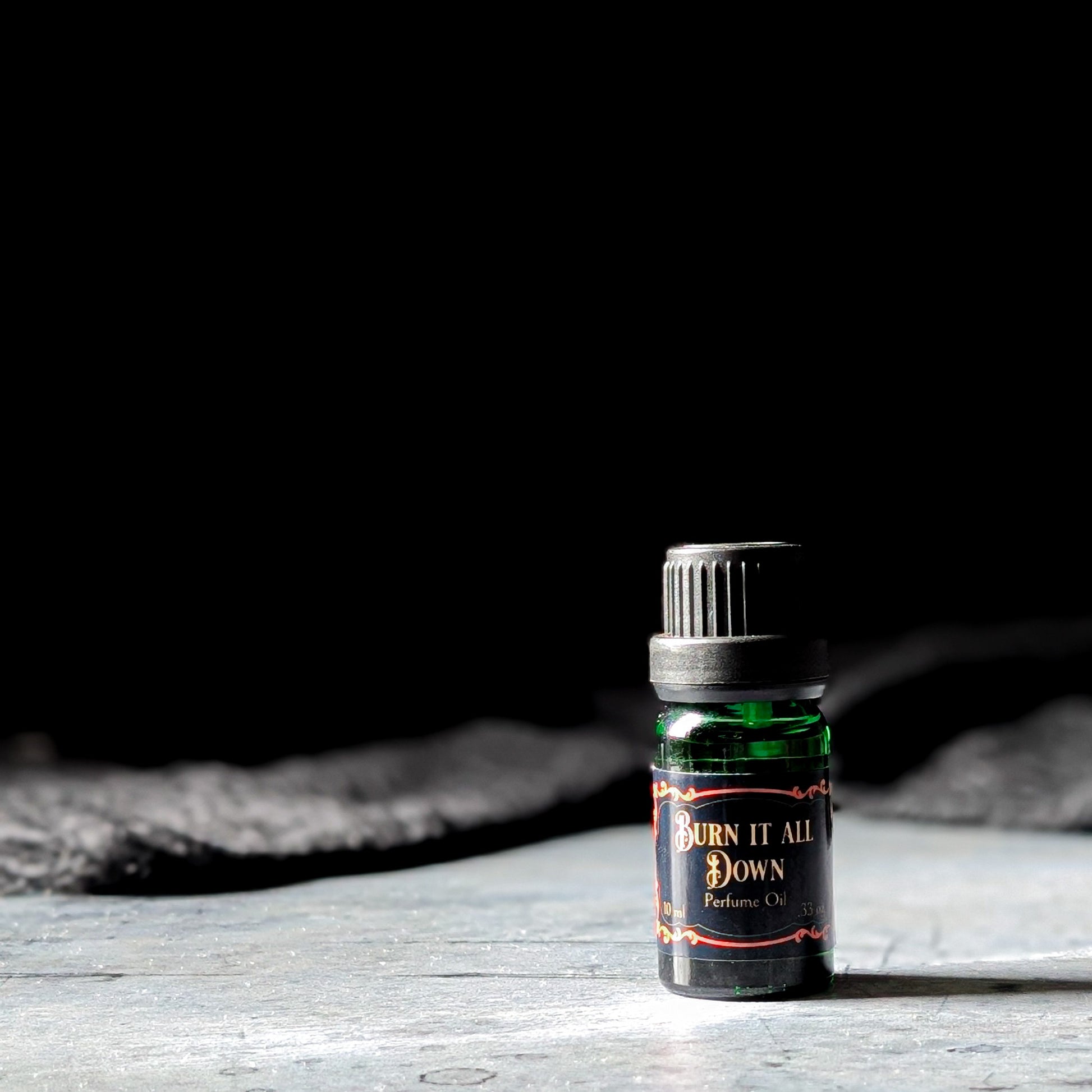 Bottle of 'Burn It All Down' perfume oil on a wooden surface with a dark background