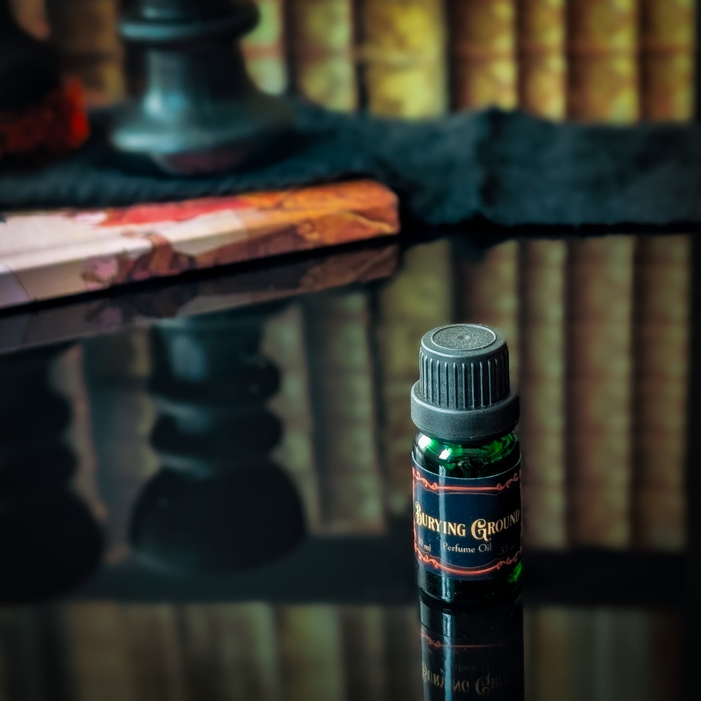 Small bottle of 'Burying Ground' perfume on a reflective surface with blurred books in the background