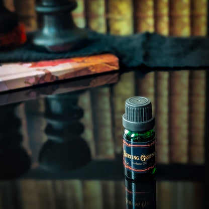 Small bottle of 'Burying Ground' perfume on a reflective surface with blurred books in the background