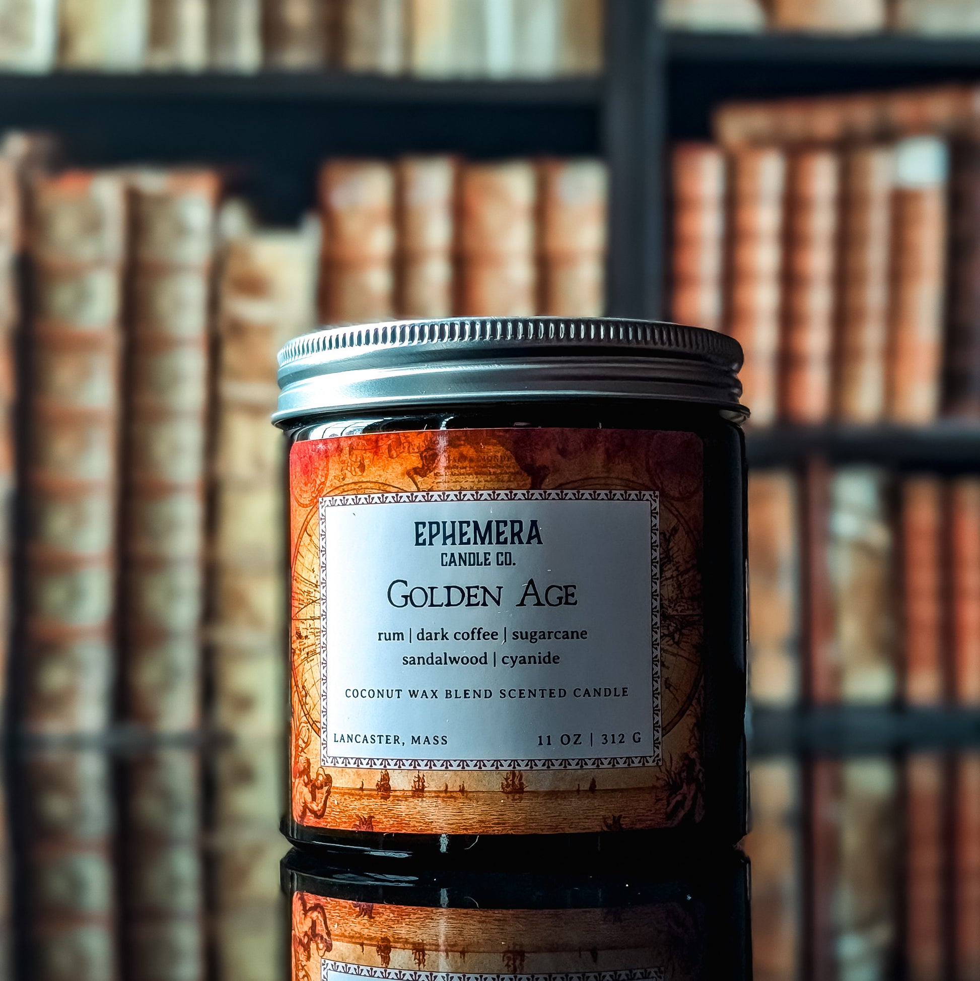 Golden Age coconut wax candle against a bookshelf background. Label is a aged map; notes rum, dark coffee, sugarcane, sandalwood, cyanide.
