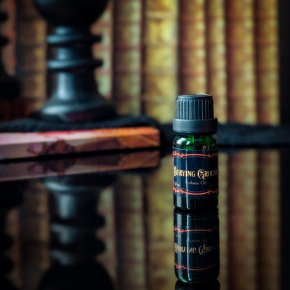 Bottle of 'Burying Ground' perfume oil on a reflective surface with blurred bookshelf in the background