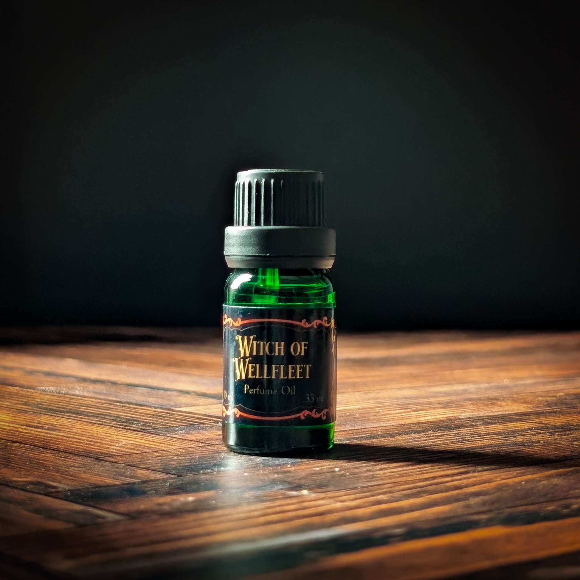 Bottle of 'Witch of Wellfleet' perfume oil on a wooden surface with a dark background