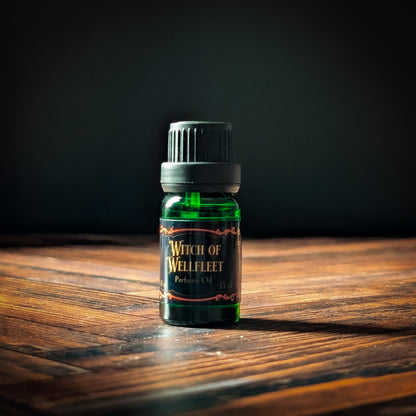 Bottle of 'Witch of Wellfleet' perfume oil on a wooden surface with a dark background