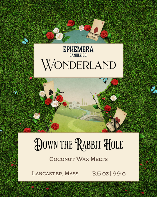 Wax melt packaging for 'Down the Rabbit Hole' by Ephemera Candle Co. on a grassy background with flowers and playing cards.